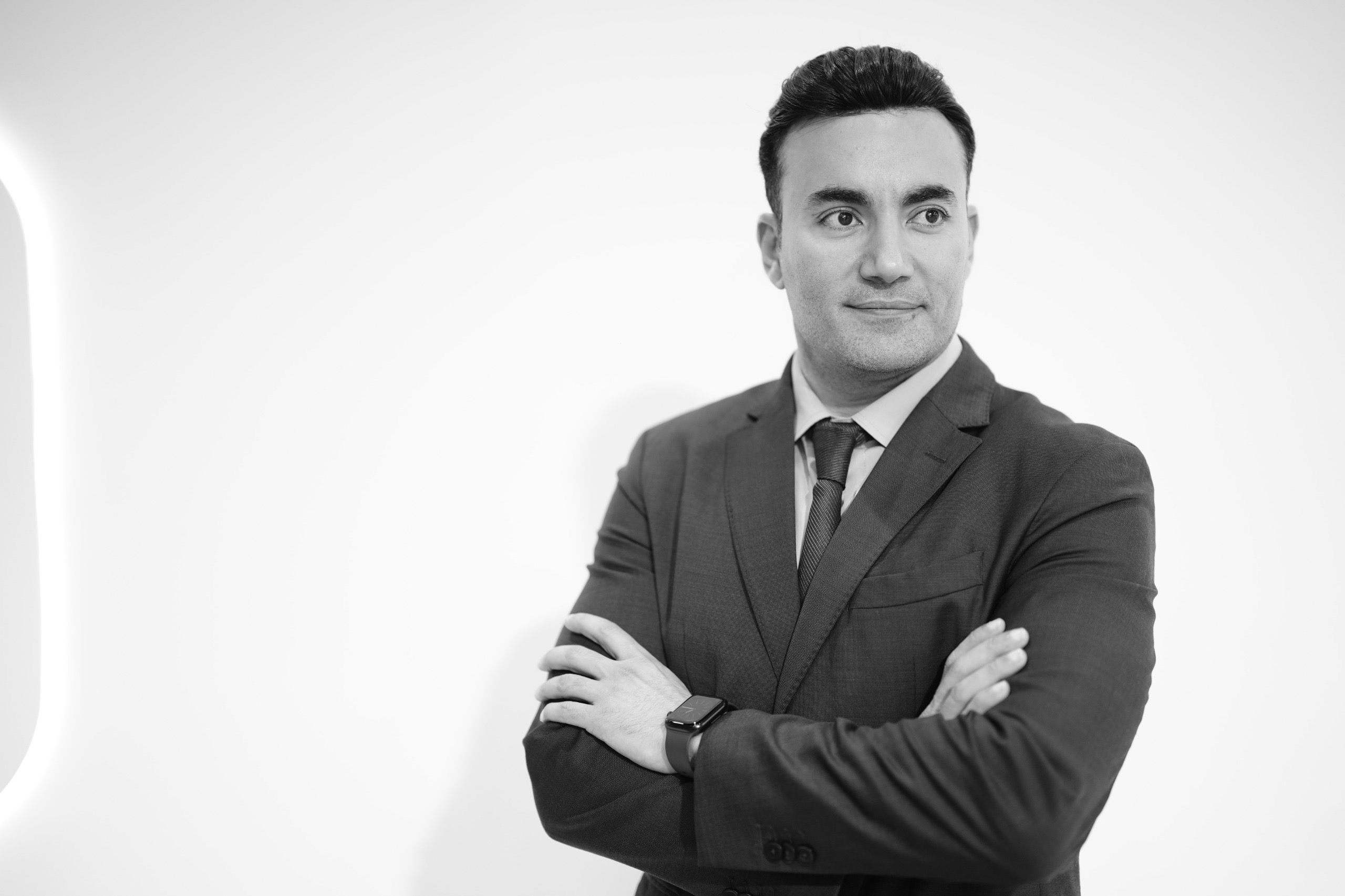 Aladdin Ismail in a dark suit and tie, arms crossed, studio portrait in black and white